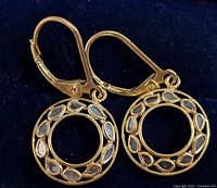Pair of gold-tone silver earrings showing circular pendants with diamond-shaped patterns and small diamonds inside each shape.