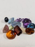 Close-up photo of 11 assorted genuine faceted gemstones in various colors and shapes on white background.