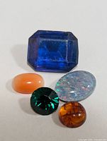 Five assorted genuine gemstones laid out, showing variety in colors, cuts, and sizes.
