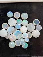 Top down view of approx 26 round genuine Australian opal cabochons with visible play-of-color effects against black background to highlight the color.