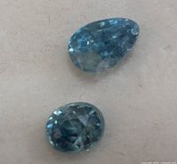 Close up photo showing oval and pear shaped blue zircon gemstones with visible facets and natural inclusions