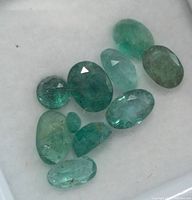 Close-up of 10 loose emerald gemstones showing color and cut variety on white background.