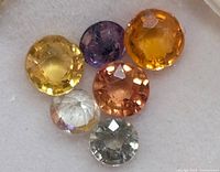 Top view of six faceted round sapphires in various fancy colors on a white background.