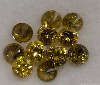 Top-down photo of twelve round brilliant cut yellow diamonds on white background.