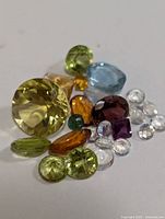 Close-up of multiple faceted gemstones of different colors and shapes on a white surface.