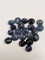 Close-up of approximately 20 loose round faceted sapphire gemstones in various sizes and blue shades.