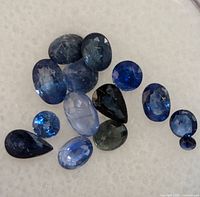 Multiple loose gemstones on white foam background showing variety of shapes and blue shades.