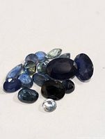 Multiple faceted sapphire gemstones in various blue shades and cuts on a white background.