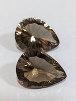 Two pear-shaped genuine smokey quartz gemstones with faceted cuts and translucent brownish-gray color viewed from above.
