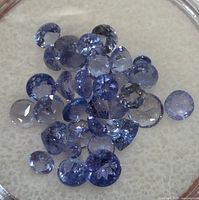Loose round cut tanzanite gemstones in various sizes and shades of blue and violet, displayed on a light surface.