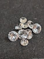 Close-up of multiple loose white sapphire gemstones placed on a dark surface, showing round faceted cuts.