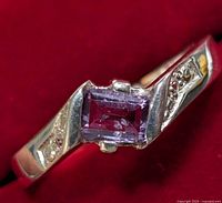 Close-up photo showing the top of the silver ring with amethyst and accent stones on a red background.