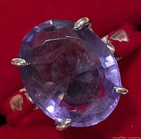 Close-up view of the oval faceted purple amethyst stone set in a silver ring with four prong settings against a red background.