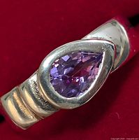 Close-up of silver ring with pear-shaped amethyst stone showing detail of gemstone and setting on a red background.
