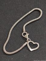 Close-up image of the silver snake chain bracelet with lobster clasp and attached hollow heart charm.