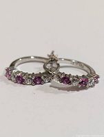 Pair of small sterling silver hoop earrings with alternating created pink sapphires and clear stones, photographed close-up to show detail of stones and metal.