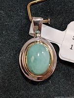 Oval sterling silver pendant with light green 1.30ct emerald cabochon set in gold-tone bezel detail.