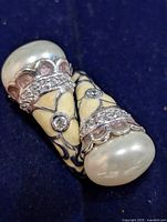 Close-up of the silver ring showing pearly ends with scalloped rose enamel edges and crystal accents on dark blue background.