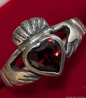 Close-up image showing the detailed Claddagh design with heart-shaped garnet stone set in silver.