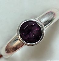 Close-up of the silver ring top showing the round purple gemstone and polished silver band.