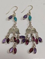 Front view of both silver multi gemstone dangle earrings displaying turquoise, amethyst, garnet, and other purple/red stones.