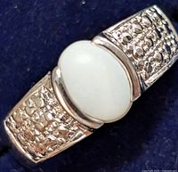 Close-up front view of silver ring with oval white opal stone and textured band.