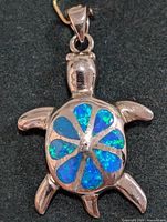 Silver turtle-shaped pendant with blue-green opalite shell inlay on black background