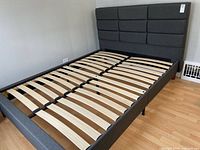 Full view of the grey upholstered bed frame with wooden slat support base and attached headboard.