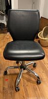 Front view of black leather look computer chair showing cushioned back and seat on metal caster base.