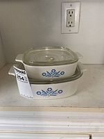 Stacked 1 litre and 2 litre Corningware casserole dishes with blue cornflower pattern and clear glass lid on top.