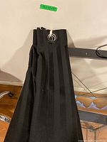 Single black drapery panel folded on table, showing large silver metal grommet and vertical stripes pattern.