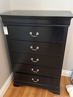Full front view of black dresser showing all five drawers and curved molding on top.