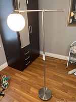 Full view of the modern floor lamp with metal body, round base, and globe shade.