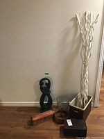 Collection arranged against wall showing all items: black plaster figure, glass bowl, two wooden baskets, nutcracker set, and tall white decorative curly branches in planter box.
