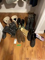 Photo from above showing six pairs of ladies boots in various styles and materials on wooden floor.