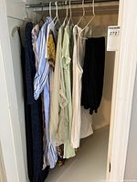 Shelf inside closet with various blouses and dresses hanging on hangers, showing multiple colors and styles including striped, floral, and solid colors.