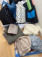 Full view of assorted linens including pillows, towels, quilt, and sheets folded and stacked on a floor