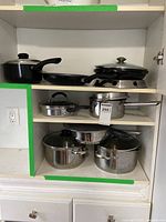Cookware arranged on shelves including stock pots, saucepans, frying pans, and wok with stand.
