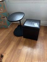 Two modern side tables together: black wooden adjustable side table and black faux leather storage ottoman