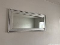 Full view of the rectangular silver framed mirror hanging on a wall, showing its size and shape