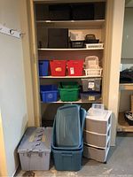 Assortment of storage containers and bins arranged on shelving and floor, including fabric bins, plastic bins, and baskets.