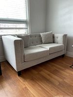 Side angle showing the sofa's off white upholstery, squared armrests and wooden legs.