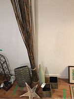 Photo showing bamboo sticks, green vase, star-shaped wooden bowl, two square candle holders on floor against wall. Also part of a silver-colored textured vase visible.