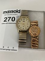 Photo showing Timex Indiglo watch with cream dial and gold-tone expandable band alongside gold tone monogrammed bracelet.