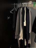 Closet space showing eight hanging items of women's sweaters and jackets in neutral tones including black, gray, beige, cream, and striped patterns.