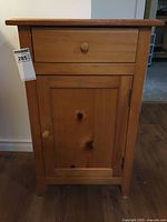 Front view of single door wooden cupboard showing drawer and door with wooden knobs and visible wood grain.