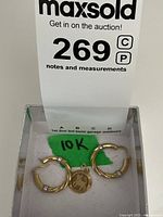 Photo of the pair of 10 kt yellow gold hollow hoop earrings with white gold accents next to a lot label showing the 10K marking on a green tag.