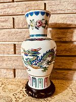 Front view of the vase showing the colorful dragon on the curved body and floral accents on the neck, placed on a carved wooden stand.