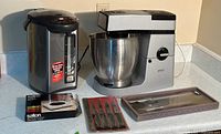 Overview of all items on counter: Kenwood Major mixer, water boiler, Salton coaster warmer box, steak knives package.