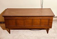 Front view of the entire wooden blanket box showing the mid-century design with paneling and angled legs.